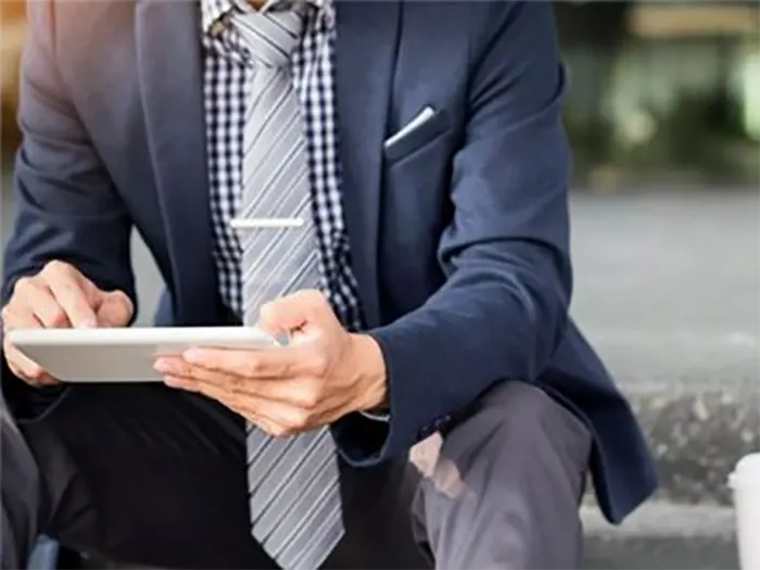 3Umwobusinessmansittingoutdoorsbrowsingontabletwithcoffeecuponthesidesuggestingabreakoroutdoorworksetting 1